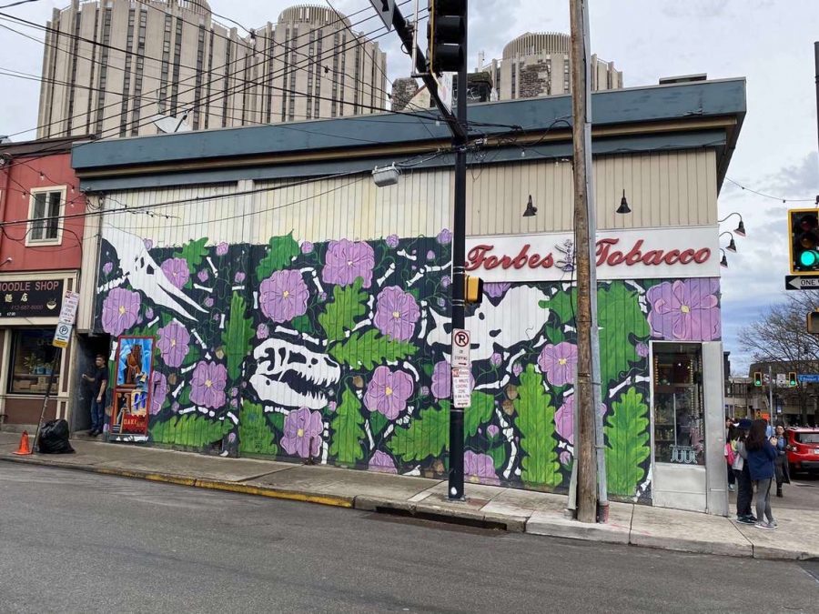 A unique mural displayed on the side of the Forbes Tobacco shop in oakland, that features dinosaurs, purple flowers, and green leaves.