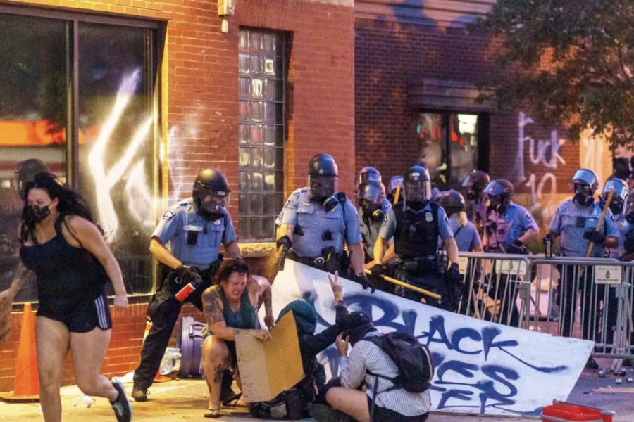 Police mace protestors sitting down holding a Black Lives Matter sign.
