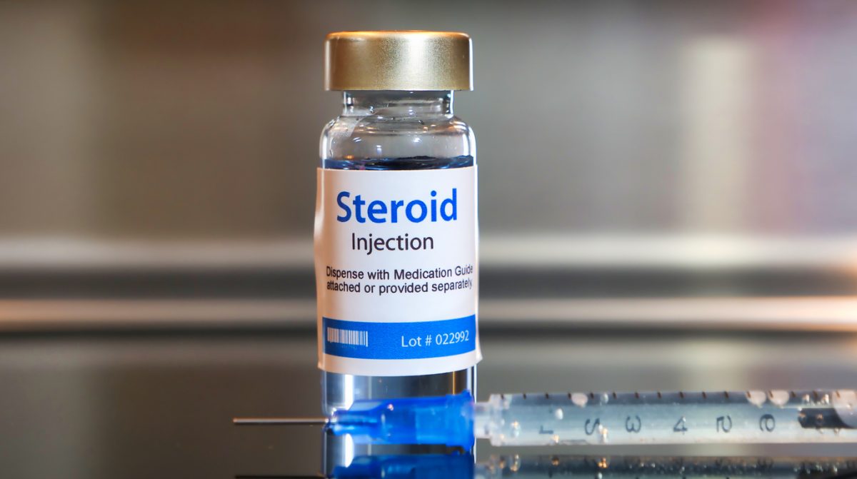 Vial of Steroid injection with a syringe on black table and stainless steel background.