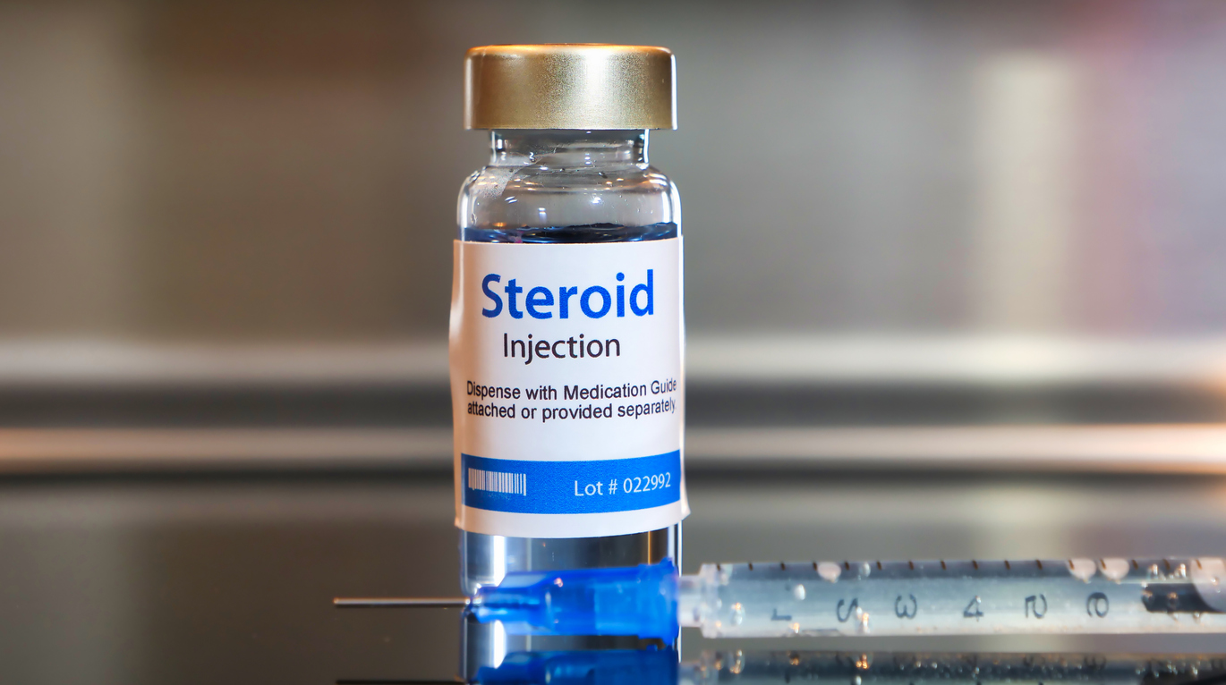 Vial of Steroid injection with a syringe on black table and stainless steel background.